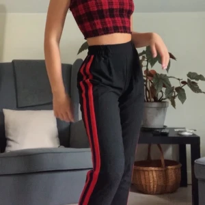 Svarta kostymbyxor med ränder - Snygga svarta kostymbyxor från Bershka med röda & marinblåa ränder. Det är resår i midjan och längden passar mig perfekt som är 160! Buda💕💕