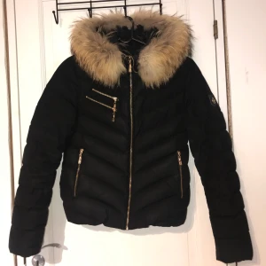 Hollies Chatel Gold äkta päls  - Storlek 38 men passar även om du har storlek 36! En stor innerficka och leopardmönstrad insida. Två stängbara ytterfickor. Äkta pälskrage (tvättbjörn). Använd en vinter. Nypris: 3499 kr Säljer för: 1000 kr 