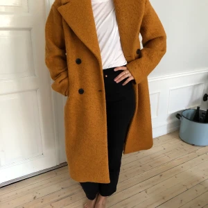 Y.A.S oversized kappa stl. S - Oversized kappa från Y.A.S i en underbar orangebronsig höstfärg. Yttertyg i 50% Ull och 50% polyester. Innertyg i 100% polyester. Storlek S men passar S ,M eller L beroende på hur man vill att den ska sitta. Kan skickas, fraktkostnad tillkommer.