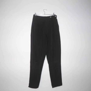  - Svarta kostymbyxor med hög midja. Dragkedja och knapp i fram men även knappar på sidan. Fint skick!