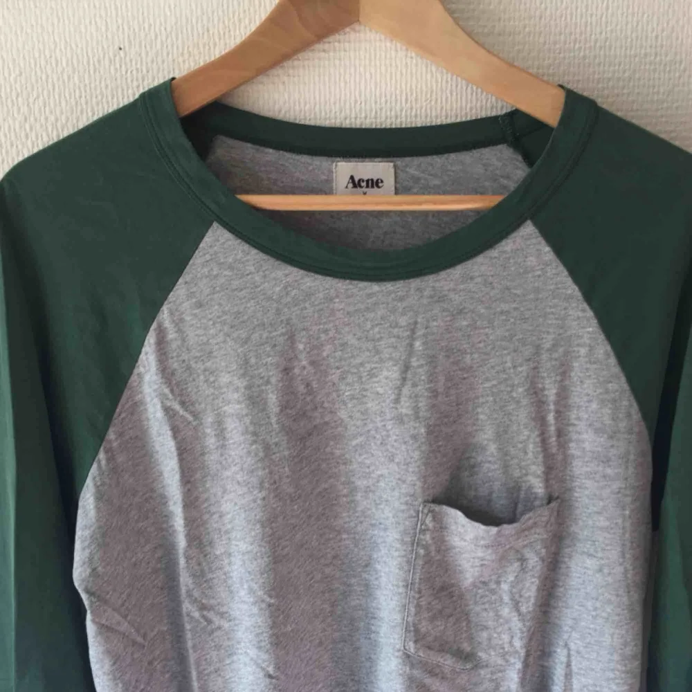 Grå/grön långärmad t-shirt från Acne. ”Baseball” modell i storlek Medium. Något länge bak (se bild). Finns ett litet hål nere i högra kanten - går enkelt att laga!  . T-shirts.
