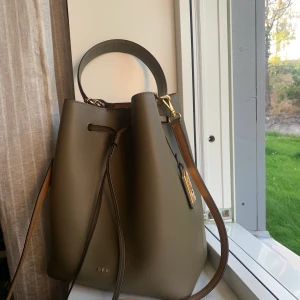 Lauren Ralph Lauren Handväska - Äkta Handväska/toutebag från Lauren Ralph Lauren. I taupe-färg. Storlek: 30cm höjd, 25cm längd. Båda band för handen och axelrem. I riktigt fint skick. (Orginalpris 3073kr)