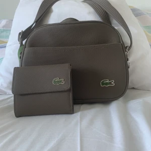 Lacoste axelväska med plånbok - Väskan och plånboken säljes ihop. Obetydligt använda. Material: konstläder 