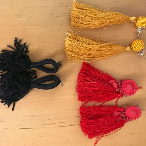 Tre par tassel/tofs- örhängen - Tre par tassel/tofs-örhängen. De Gul/oranga från Ginatricot är i princip oanvända, pris 70kr. De svarta från h&m använda ca 5 gånger, pris 60kr. De röda är från h&m lite mer använda och därmed lite slitna på framsidan, pris 50kr. Kan gå ner i pris! 