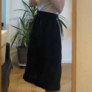 Svart monki-kjol med broderat mönster - kjol med typ broderat mönster i form av ansikten. Lite speciellt material, det är väldigt tunt och nästan lite plastigt? Vet inte men det gör att kjolen blir väldigt lätt och puffig så det är positivt! Resår i midjan så passar m-l/xl, även s med bälte til