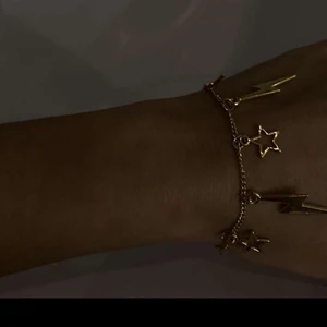 Armband, smycken  - I08. Jättefint armband med stjärnor och blixtrar i guld. Glöm inte att 10% av vinsten går oavkortat till organisationen kvinna till kvinna. 