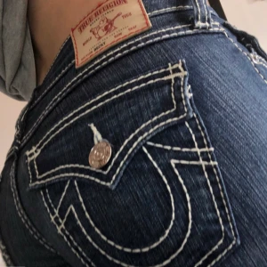 True Religion Bootcut Jeans - Lågmidjade True Religion jeans med vita kontrastsömmar. Köpt på Depop för 700 kr och aldrig använda pga att de inte passade. Perfekt skick, inga texken på användning. W26 men passar upp till W28. Köpare står för frakt. Buda gärna! DM:a vid frågor💕