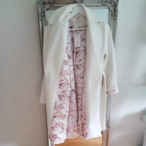 Säljer denna snygga designade vita kappan med rosablommigt mösnter på insidan från Lene Orviks kollektion från Bikbok. Helt oanvänd, prislappen är fortfarande kvar! Säljer den pga att den tyvärr inte kommer till användning.