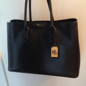  - Större väska i skinn från Lauren by Ralph lauren. Två handtag och gulddetaljer. Välbevarad. Köpt på best of brands 2016. Nypris 3125:- mindre fack inuti som försluts med magnet. Läderhasp att stänga väskan med och två större fack invändigt. 