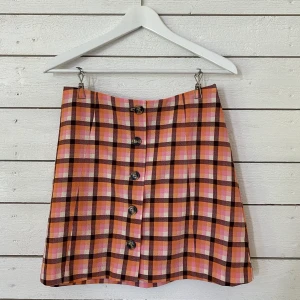 Rutig kjol från Monki - Kjol som knäpps i fram med knappar, slät baktill. Använd fåtal gånger. Skön passform och passar mig som vanligtvis har storlek S. Frakt tillkommer (42kr)