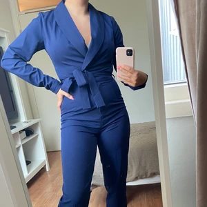Marinblå byxdress - Mörkblå byxdress/jumpsuit i kostymliknande modell, köpt på Zalando. Knäpps fram med både gylf och knappar. Avtagbart skärp. Nyskick, använd endast en gång. Köparen står för frakten.