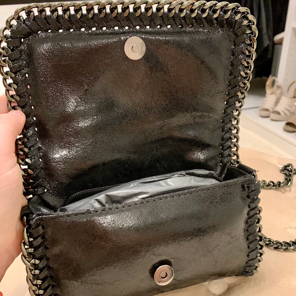 NY. Helt oanvänd jättefin svart väska i äkta skinn med mörk metallkedja. Liknar Stella McCartneys falabella miniväska. Avtagbar kedja, väskan kan användas som clutch också. Mått: 22x13 cm. Köpt i Marbella. . Väskor.