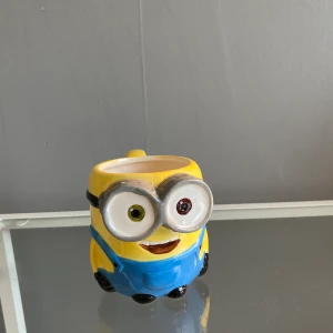 Minion mugg - Porslins mugg i form av en minion. Köpte i en butik i Spanien. Använt fåtals gånger, har använt den som prydnad. Pris kan diskuteras 