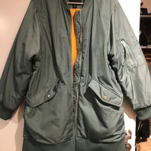 Grön bomberjacka  - Lång bomberjacka som är använd sparsamt finns ett litet litet hål i ena armen 