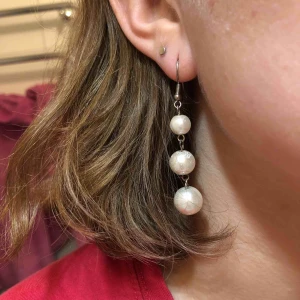  - Örhängen med plastpärlor i tre olika storlekar. En vit glansig pärlfärg i grunden med ett vitt abstrakt mönster på. 