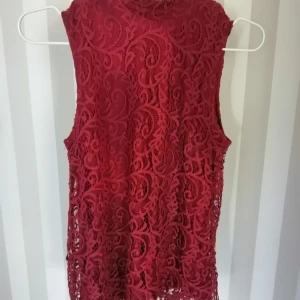 Vinrött Linne med spets och hög krage - Ett mjukt följande linne med ett underlager av viskos och ett övre av virkad polyamid. Lite högre krage samt dragkedja bak i nacken som går ner ca 2 dm. 