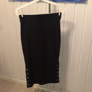 Ribbad kjol - Svart ribbad kjol med fem öppningsbara knappar på vardera sida. 