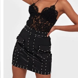 Svart kjol med nitar storlek Medium - Två fickor framtill och dragkedja bak. Är själv storlek S och denna som är M sitter perfekt så kjolen är aningen liten i storlek. Kjolen är fodrad och materialet är någon typ av läder/skinnimmitation. Helt ny och oanvänd