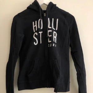 Hollister hoodie - En marinblå huvtröja med dragkedja från Hollister. Använd en del men inte trasig eller fläckig. I storlek XS men passar även S