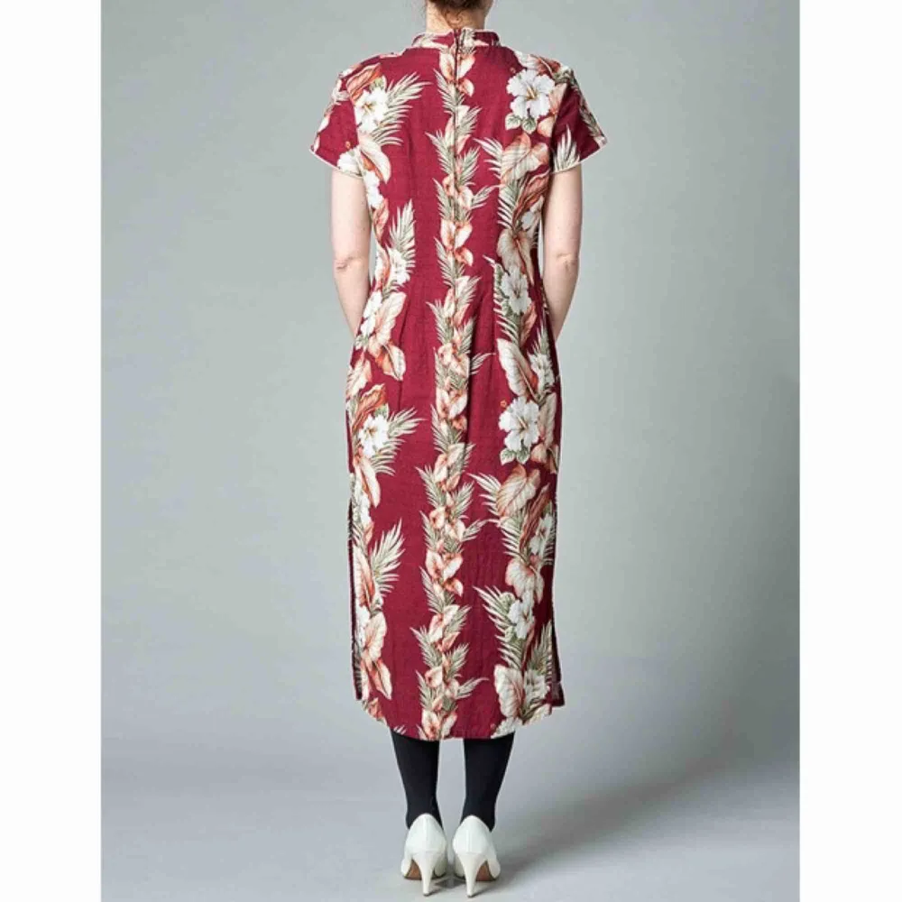 En hawaii-klänning med kinakrage. Slits i båda sidor, axelvaddar och vit passpoal runt ärm och krage. Mäter 116 cm från axel. . Klänningar.