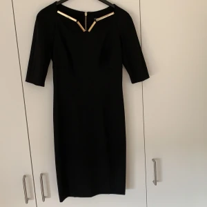 Klassisk svart klänning - Underbar svart klänning i stretch kvalite med guld detaljer. Köpt i Rom. Använt ca. 2 gånger.
