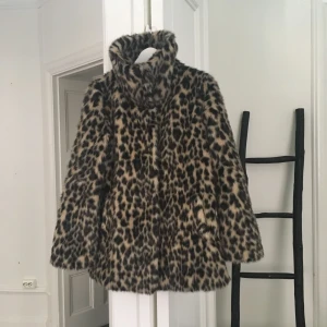  - Fuskpäls leopardmönstrad. Superfint skick. Endast ett litet hål i höger ficka och en av knapparna sitter löst, men lätta saker att åtgärda. Varm och mysig, stor härlig krage. Någorlunda figursydd. 