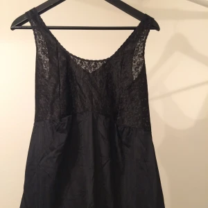  - Svart klänning i tunt material med spets över bröst. 