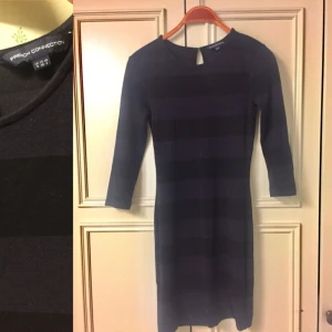  - Randig klänning i 83% viskos från French Connection i mycket fint skick. Mycket mjuk och tjock tyg. Svart mörkblå/ lila, längden på framsidan är 77 cm. Storlek är en 36 som sitter nära kroppen. 3/4 ärmen.  Från djur- och rökfri hem.