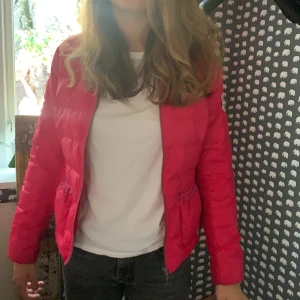 Dunjacka  - En oddmolly jacka i storlek 1 som är rosa. Den har volanger på fickorna. 