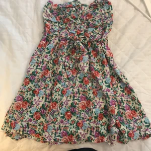 Blommig miniklänning  - Klänning i blommigt mönster. Använd fåtal gånger. Knappar som detalj framtill och knytband i midjan.