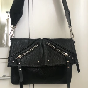 Axelremsväska - Svart axelremsväska från don Donna med band från Carin Wester. Väskan är rymlig och har innerfack. Den är i fint skick!