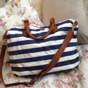  - Sailorinspirerad handväska. Rymlig. Axelremmen är avtagbar. Fack med dragkedja på utsidan. Fack med dragkedja på insidan, samt två fack utan dragkedja.  Bredd: 45 cm Höjd: 30 cm Djup (botten): ca 18 cm