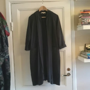  - mörkgrå tunn vår/sommarkappa från Carin Wester. läderband som kan knytas i ryggen eller runt midjan. mkt bra skick men lite trasig söm som ses på bild nr 3. 