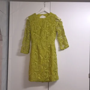  - Jättefin spetsklänning med öppen (rund) rygg. Olivgrön. Dragkedja baktill och knäppning vid nacken. 
Oanvänd, prislapp kvar! 
OBS! Liten i storleken, mer som än 34. 
