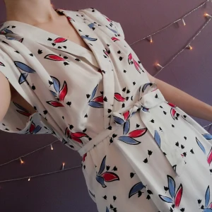 Vintage Klänning  - Vit vintage Klänning med omlott liknande detalj och resår i midjan. Skärp medföljer. Väldigt bra skick Pris diskuterbart