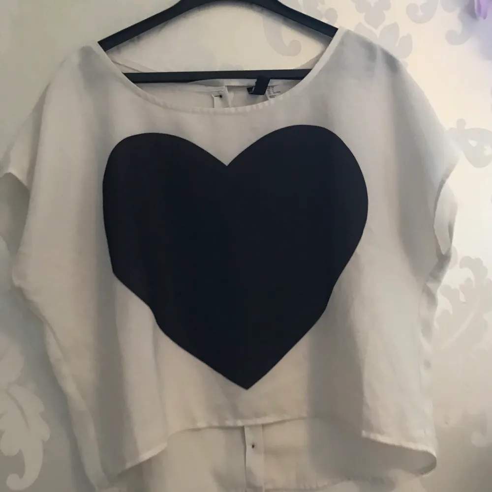 En vit blus med ett svart hjärta och kappar bak, vid ryggen från H&M i storlek 36. Blusar.