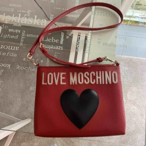  - En liten röd LOVE MOSCHINO väska. Axelbandet är reglerbart och väskan är i bra skick. De vita bokstäverna är lite smutsiga men ingenting som inte kan gå bort. Bra storlek som får plats med det viktigaste. 