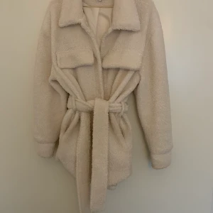 NAKD oversize teddyjacka - Säljer denna fina gräddvita oversizejackan i teddy. Den har ett skärp i midjan som skapar en snygg siluett. Knappt använd. Passar strlk 36-40 beroende på hur man vill att den ska sitta