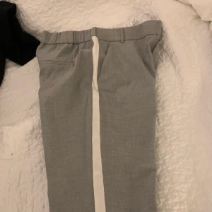 Gråa kostymsbyxor från Zara i storlek L  - Gråa med vit linje på sidan, slutar vid fotleden och bekväma vid midjan pga resårbandet. Köpta från Zara i jättebra skick, använt de fåtal gånger. Väldigt stretchiga, passar M-L.
