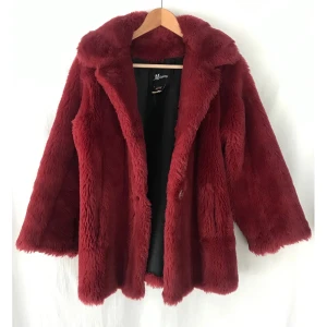 Fauxfur Pälsimitation mörkröd jacka 38/40 - Cosy fauxfur pälsimitation jacka i mörkröd färg. Storlek US Size 10 (st.38/40), flexibel i storlek. Fint skick och inget att anmärka på. Köpt i vegan friendly designers butik i USA. Tre knappar och två fickor. Svart syntetiskt foder. Längd: 69cm  Material: syntetiskt päls