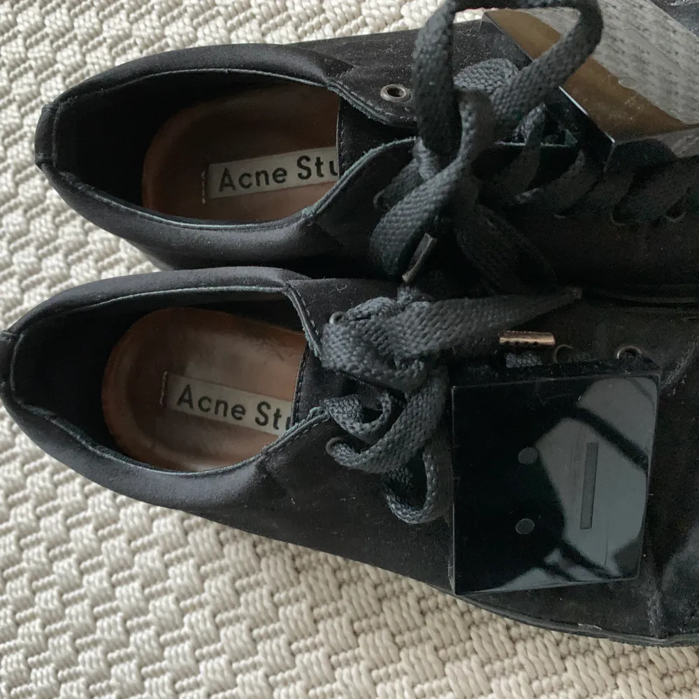 Svarta sneakers från Acne Studios i silkigt material och med den klassiska loggan!  Så snygga skor men har för många svarta så hoppas någon annan får mer användning av dem.  De är använda men fortfarande sjukt fina, fråga för mer bilder 🥰. Skor.
