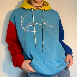 Oversized blå, röd & gul Karl Kani färgglad color block hoodie  - Ljusblå oversized Karl Kani color block hoodie med gul luva, röd högerärm, en rymlig ficka och mörkblå vänsterärm med Karl Kani broderat i vit tråd på bröstet 🧵 Så skön passform för att antingen bara ha på sig hemma men också till ett par jeans, matchande blå, gula eller röda huvudaccessoar och ett par skor som matchar (vilket basically kan vara allt från vanliga vita sneakers till ett par dr martens vars gula tråd matchar luvan perfekt!) Hoodien är markerad som en storlek M men har en oversized fit vilket gör att den passar alla men kommer naturligtvis sitta olika på person till person! Snöret är inte original utan är utbytt!