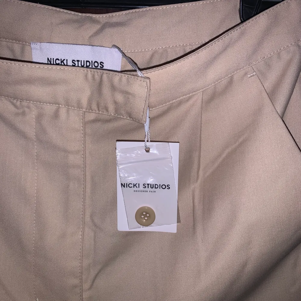 Säljer ett par NICKI STUDIOS ”Nude Shell Shorts” i storlek S. Shortsen har två fickor med knappar bak. 70% polyester 30% viskos. Oanvända med prislapp kvar. Kan mötas upp i Uppsala eller frakta mot kostnad 🧊🤩💞. Shorts.