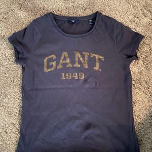 En marinblå T-shirt från Gant med guldiga tryck skrivit Gant. Använd få gånger och är i storlek xs 
