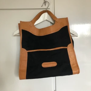 Handväska med skinndetaljer - En handväska i tyg med skinndetaljer, slitna handtag. SAMFRAKTAR