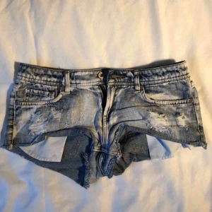  - Blåa jeansshorts med slitningar och vita ”fläckar”. Är i använt begagnat skicka men inga fläckar eller liknande. Köparen betalar frakten