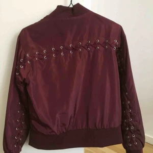  - Bombarjacka från NA-KD i gott skick, vinröd i storlek S, med snörning på ryggen. Grymt snygg men kommer tyvärr ej till användning!