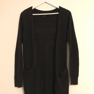  - Svart långkofta med knäppning och struktur i tyget. Litet dammig då den legat med ylle, och en ficka har lossnat lite i sömnen. Annars fint skick!