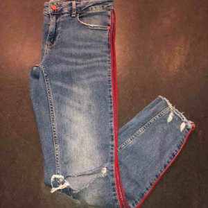 Jeans med rivär - Jättefina skinny jeans med hål på slitningar och röd rivär på sidorna, lågmidjade. Säljer dem för att dom är försmå för mig. Fint skick och som sagt väldigt fina. Köparen står för eventuell frakt. 
