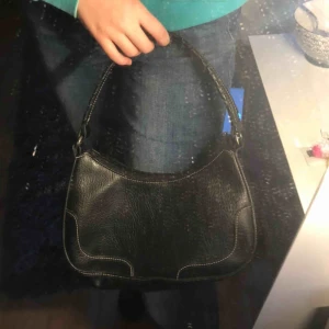  - Svart väska som man har över axeln. Köpt second hand. Brukar ha den med den helt svarta sida utåt.